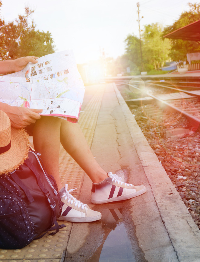 Eine Person sitzt am Bahnsteig und plant eine Reise mit einer Karte.